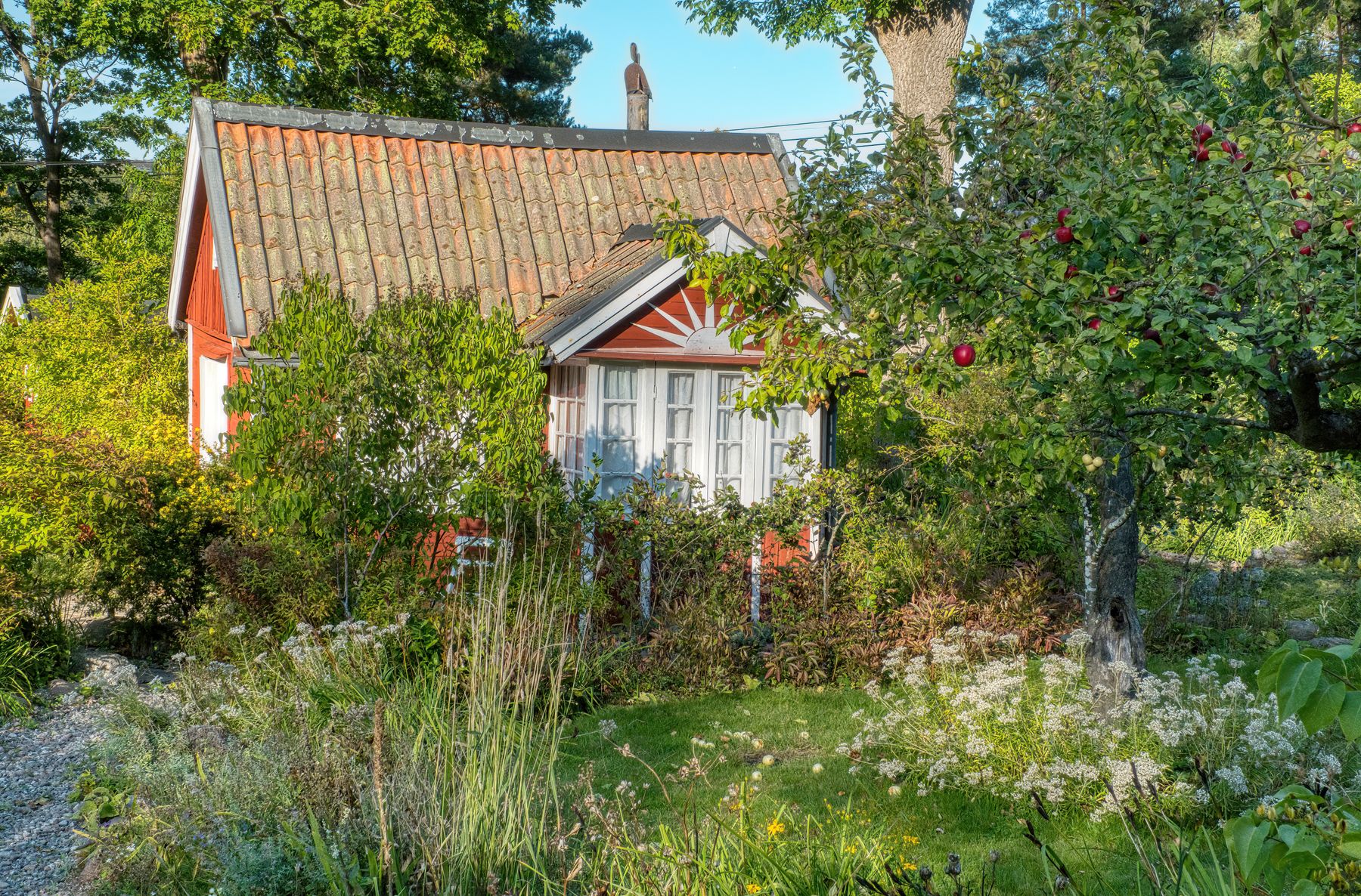 A red garden cottage framed by fruit trees and greenery