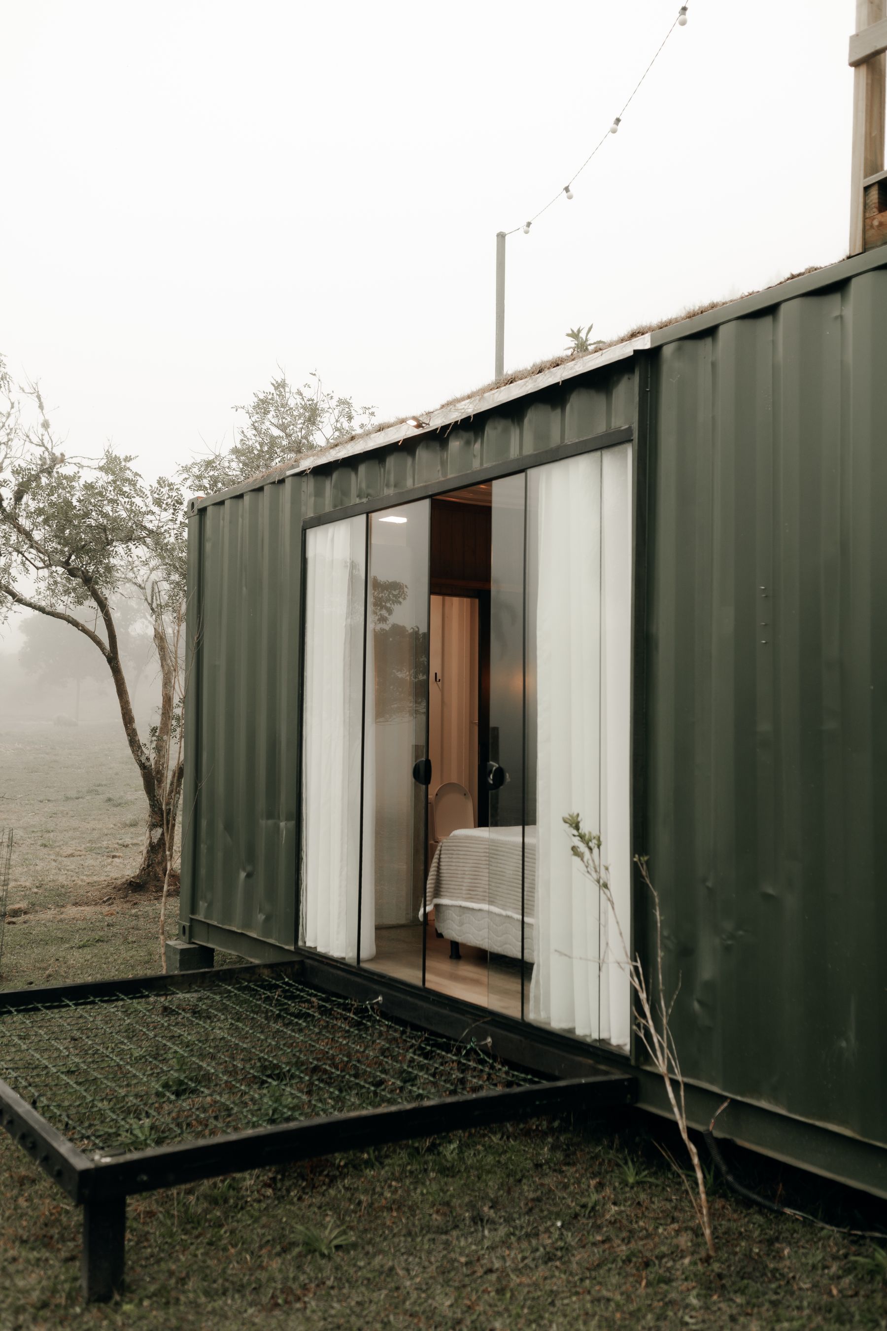 Green container home with wide glass doors in a misty landscape